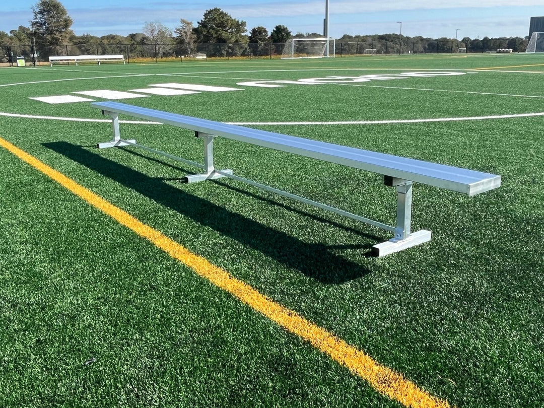 A lightweight aluminum soccer team bench placed on a grass field with a sports field's worth of background.